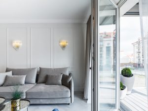 Living room with open balcony showcasing single hinged doors and grey sofa, enhancing the bright and airy space.