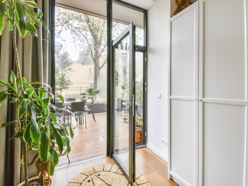 Open single hinged doors in a living space leading to an outdoor deck, highlighting natural light and greenery.