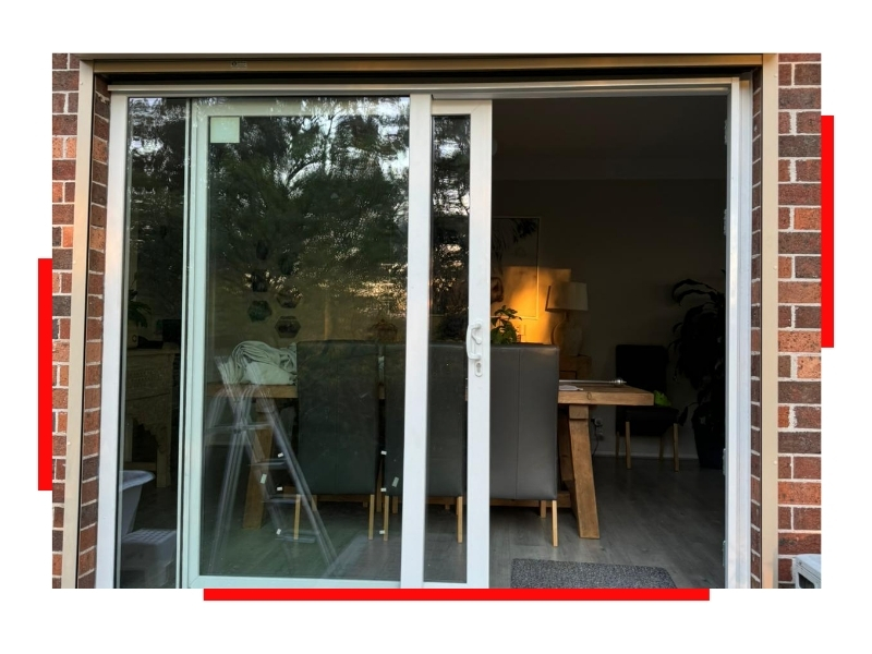 Exterior view of a living room through sliding glass doors framed by red-bricked walls.