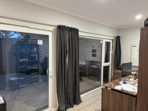 Home office area with sliding glass doors opening to the backyard, covered with black curtains.