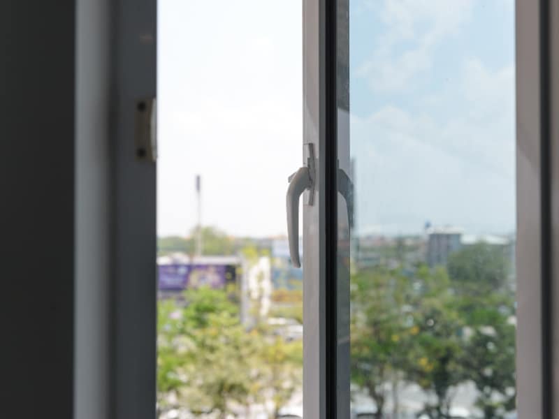 A close-up shot of a white frame showcasing upvc tilt turn windows, looking out to a cityscape with trees.