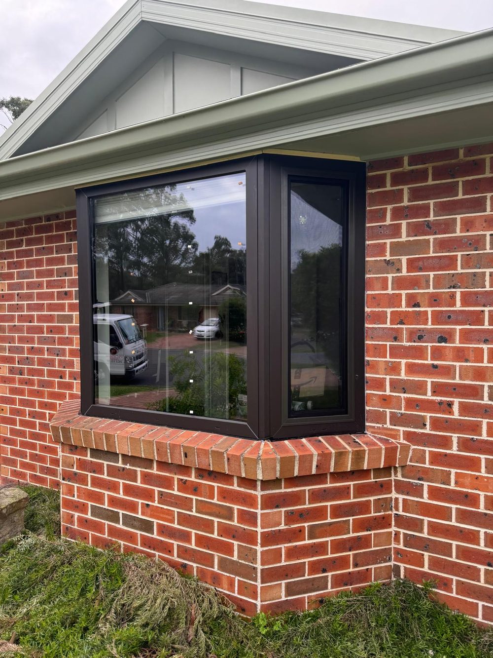 Dark framed uPVC bay window installed in the red brick wall of an Australian coastal home, viewed from the garden