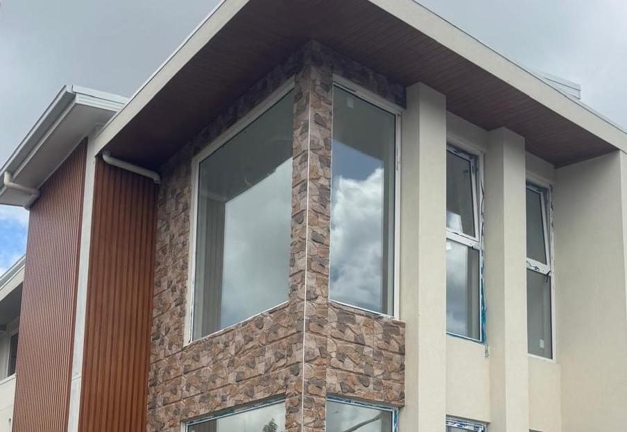 Two storey Australian home with large dark framed uPVC windows and stone cladding set against a cloudy sky