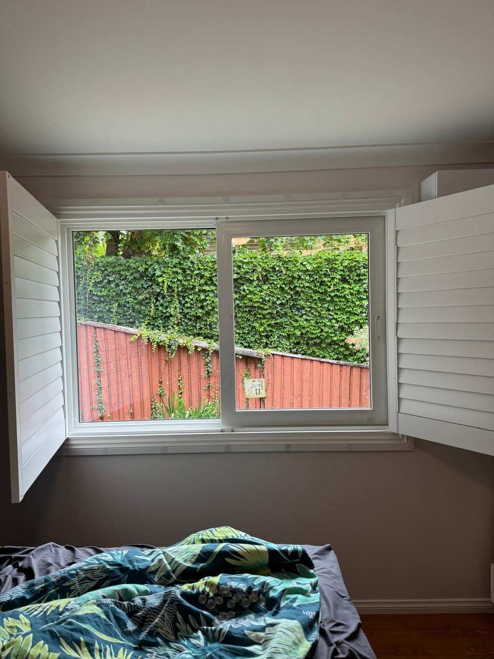 White uPVC sliding window with plantation shutters in a bedroom of an older Australian home