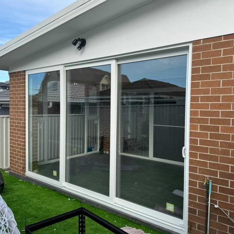 Large white uPVC sliding door across the back of a brick home opening to a lawn and paved area