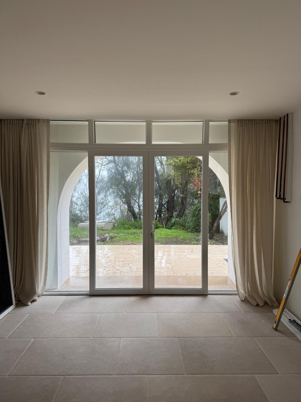 Tall white uPVC sliding door with curtains either side opening onto a paved garden in an Australian home